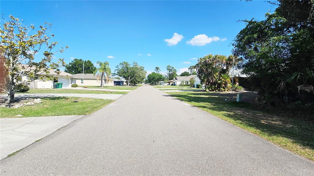 A paved residential street stretches between houses, palm trees, and lush green landscaping under a sky — 23039 & 23047 AUGUST LOTS 24 & 25 AVENUE, PORT CHARLOTTE, FL