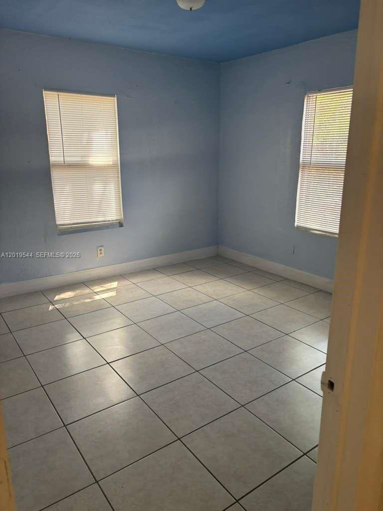 An empty bedroom features light blue walls, a tiled floor, and two windows with blinds — 1447 NW 98th St # 0, Miami FL 33147, MIAMI, FL