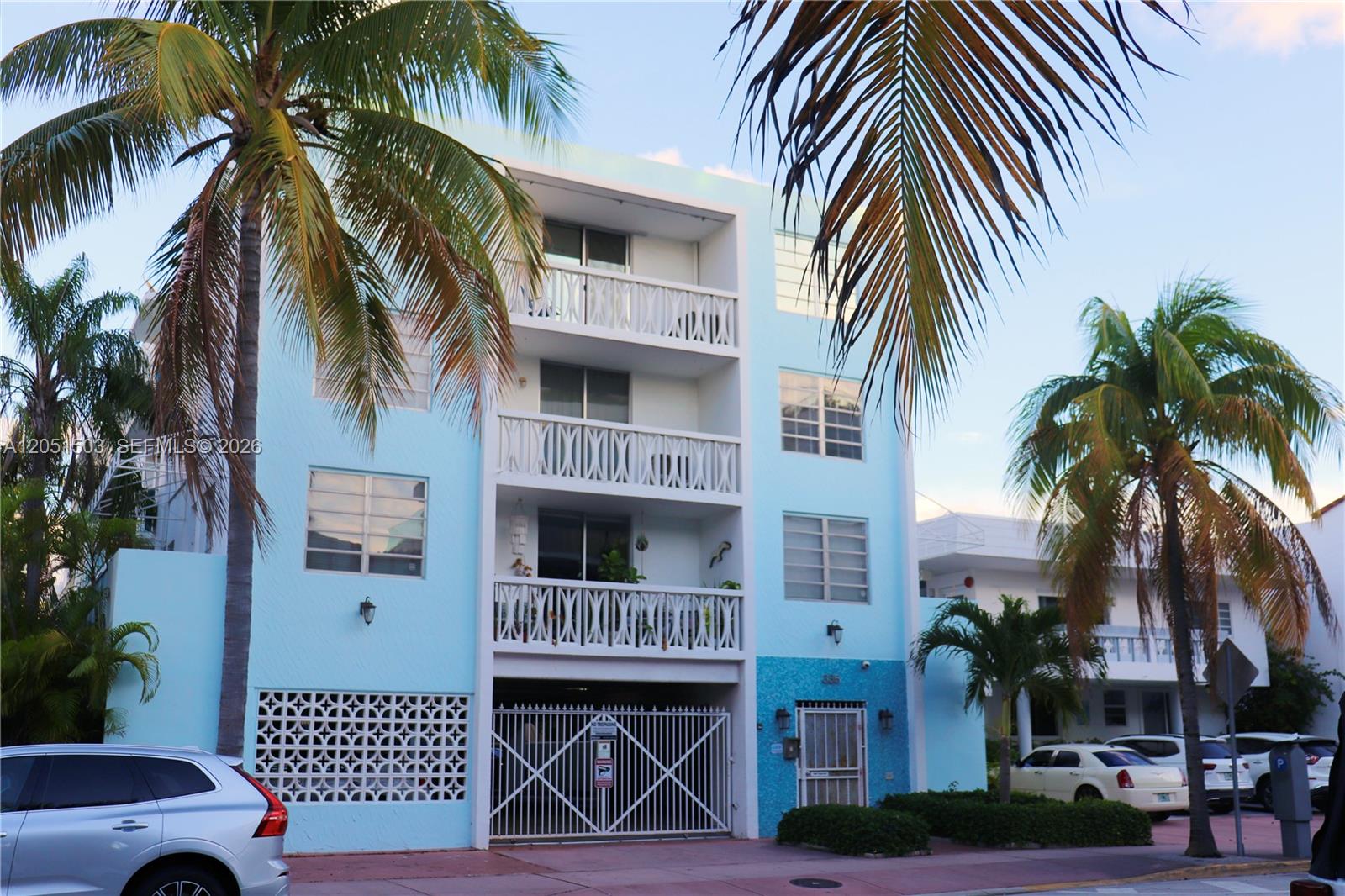 A light blue three-story apartment building features white balconies and a gated ground-level parking area — 335 Collins Ave # 203, Miami Beach FL 33139, MIAMI BEACH, FL