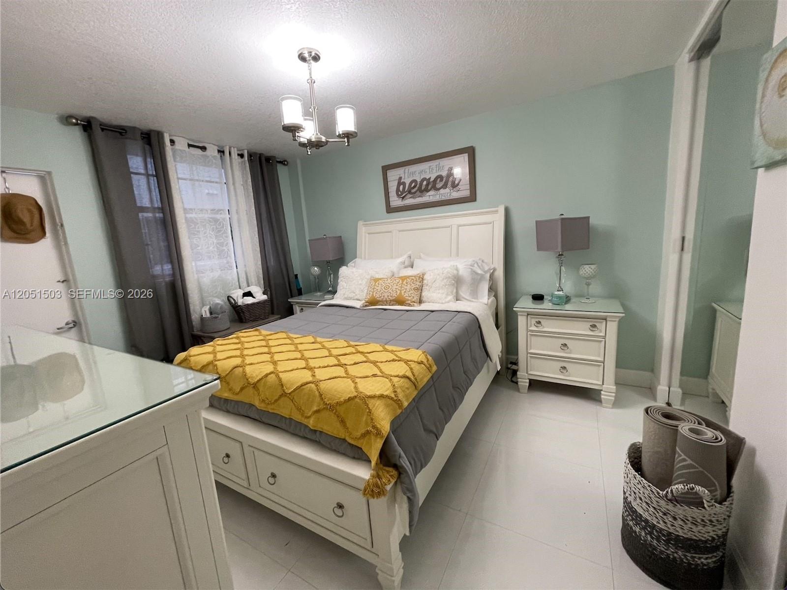A bedroom features a white bed with a yellow throw, light blue walls, and tile flooring — 335 Collins Ave # 203, Miami Beach FL 33139, MIAMI BEACH, FL