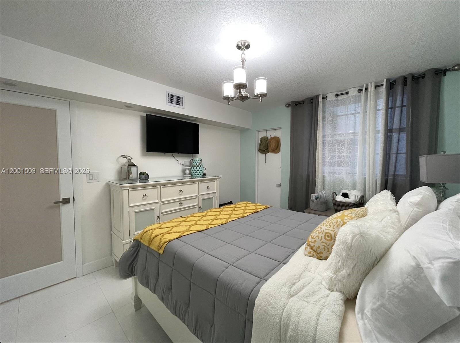 A bedroom features a gray bed with a yellow runner, white dresser, and wall-mounted television — 335 Collins Ave # 203, Miami Beach FL 33139, MIAMI BEACH, FL