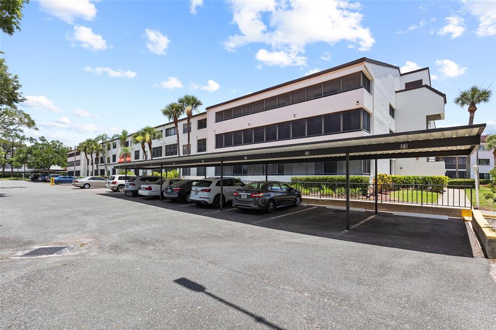 A multi-story apartment building features a covered parking area with numbered spaces in front — 2587 COUNTRYSIDE BOULEVARD UNIT 6110, CLEARWATER, FL
