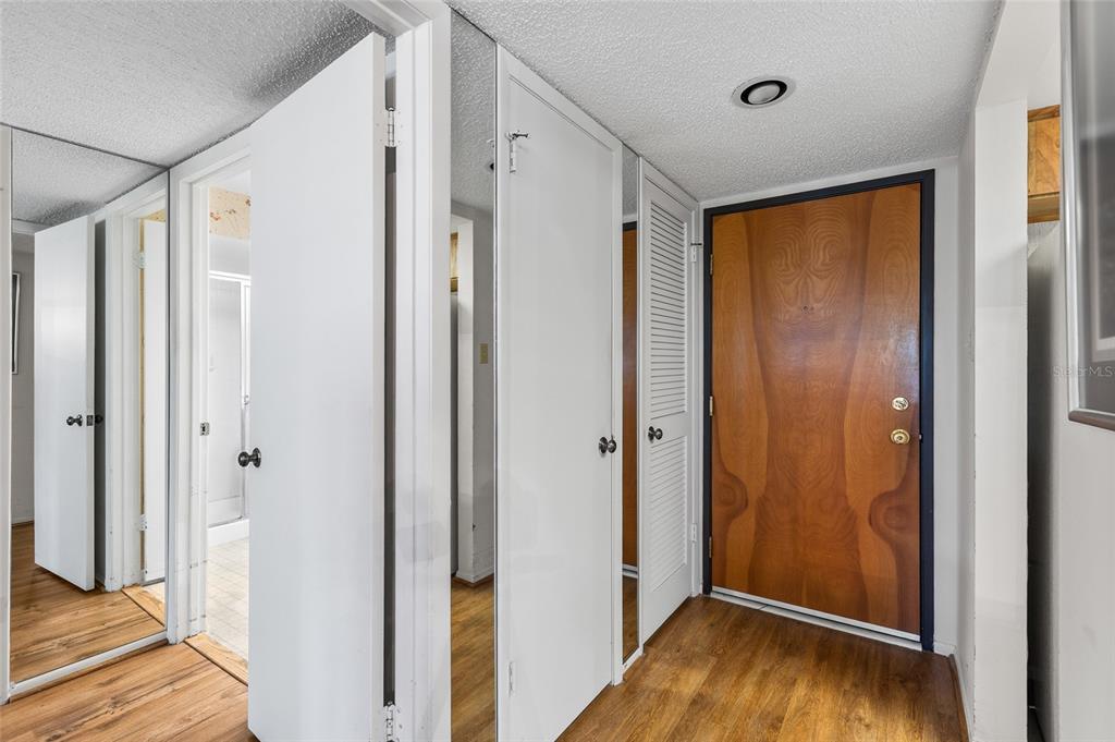 A hallway features wood-look flooring, a wooden front door, and several white closet doors — 2587 COUNTRYSIDE BOULEVARD UNIT 6110, CLEARWATER, FL