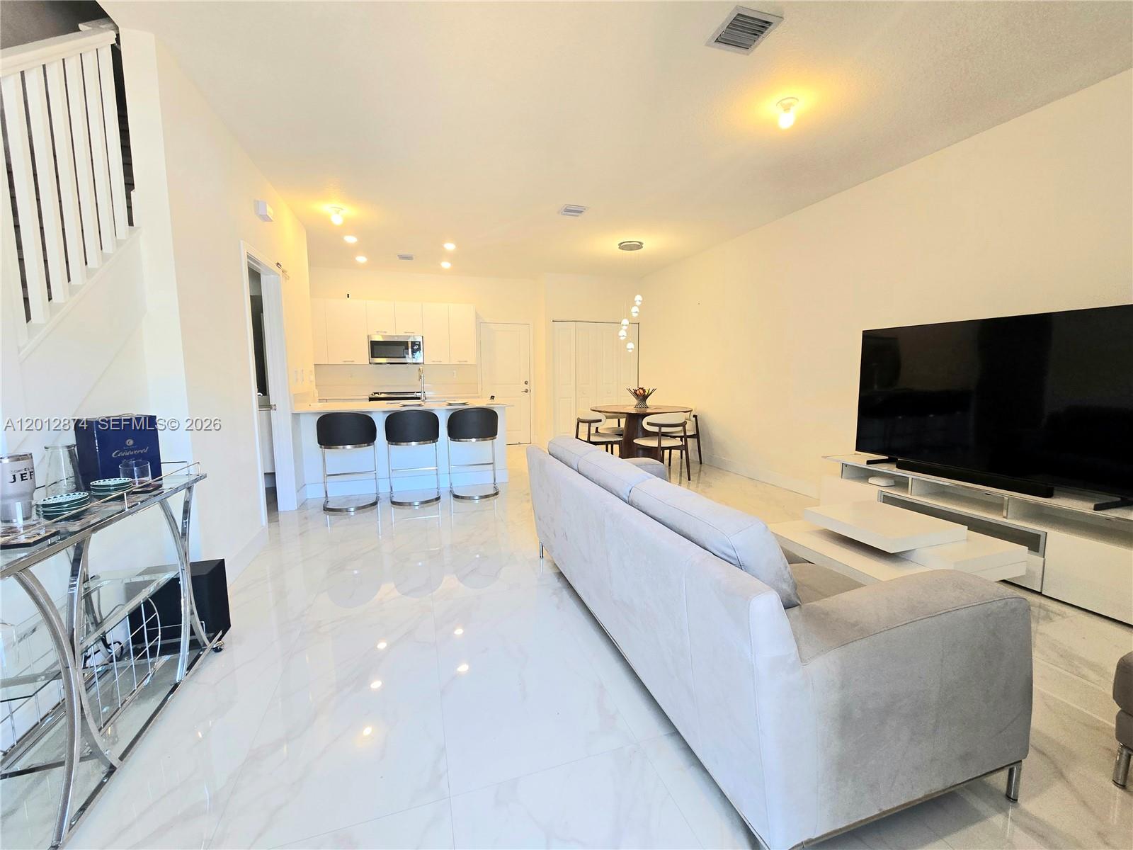 An open-concept living room and kitchen feature white cabinetry, marble-look tile flooring, and modern furniture — 4278 NW 82nd Ave # 4278, Doral FL 33166, DORAL, FL