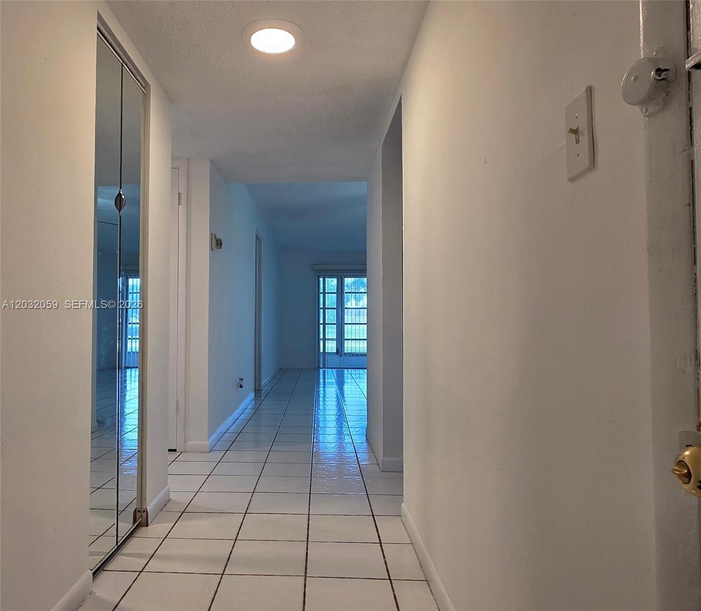 A hallway with white tiled floors leads toward a glass sliding door — MARGATE, FL