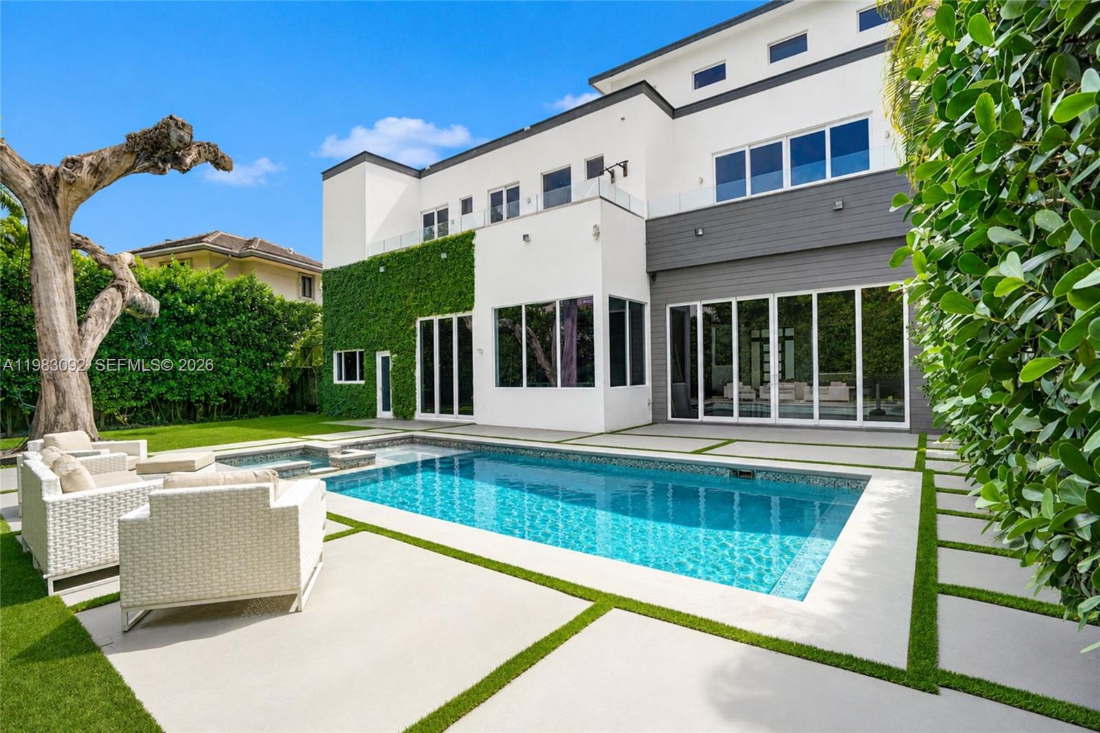 A modern two-story house features a swimming pool, patio, and a wall covered in ivy — 19914 NE 19th Ct, Miami FL 33179, MIAMI, FL