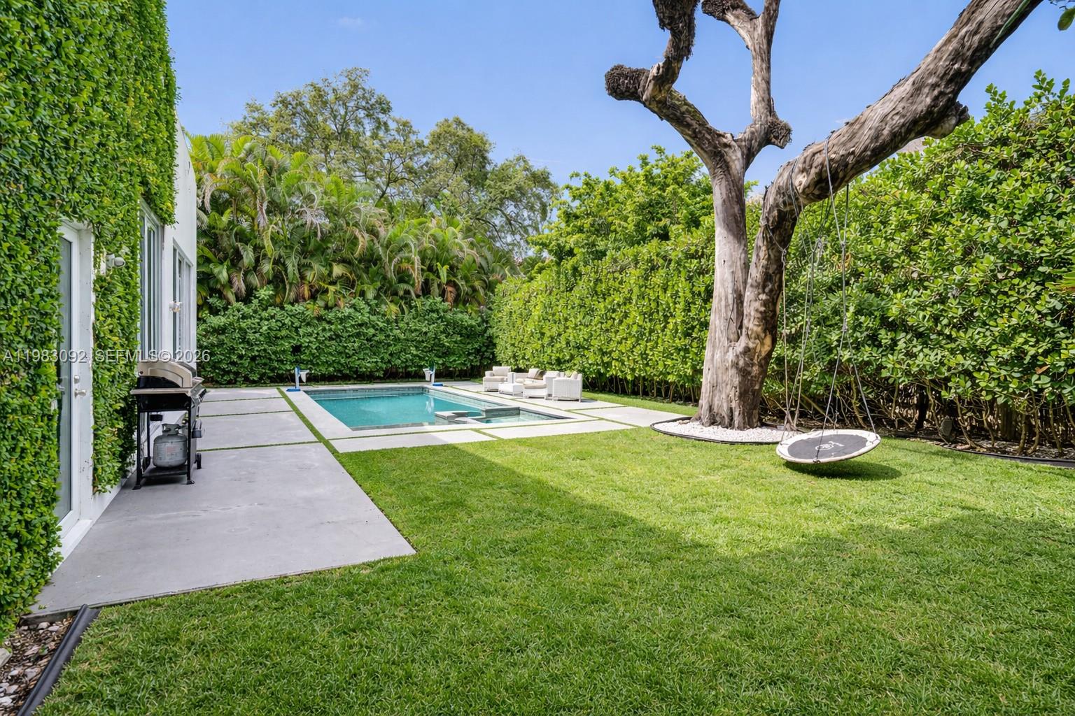A backyard features a swimming pool, a grassy lawn, a large tree with a swing, and hedges — 19914 NE 19th Ct, Miami FL 33179, MIAMI, FL
