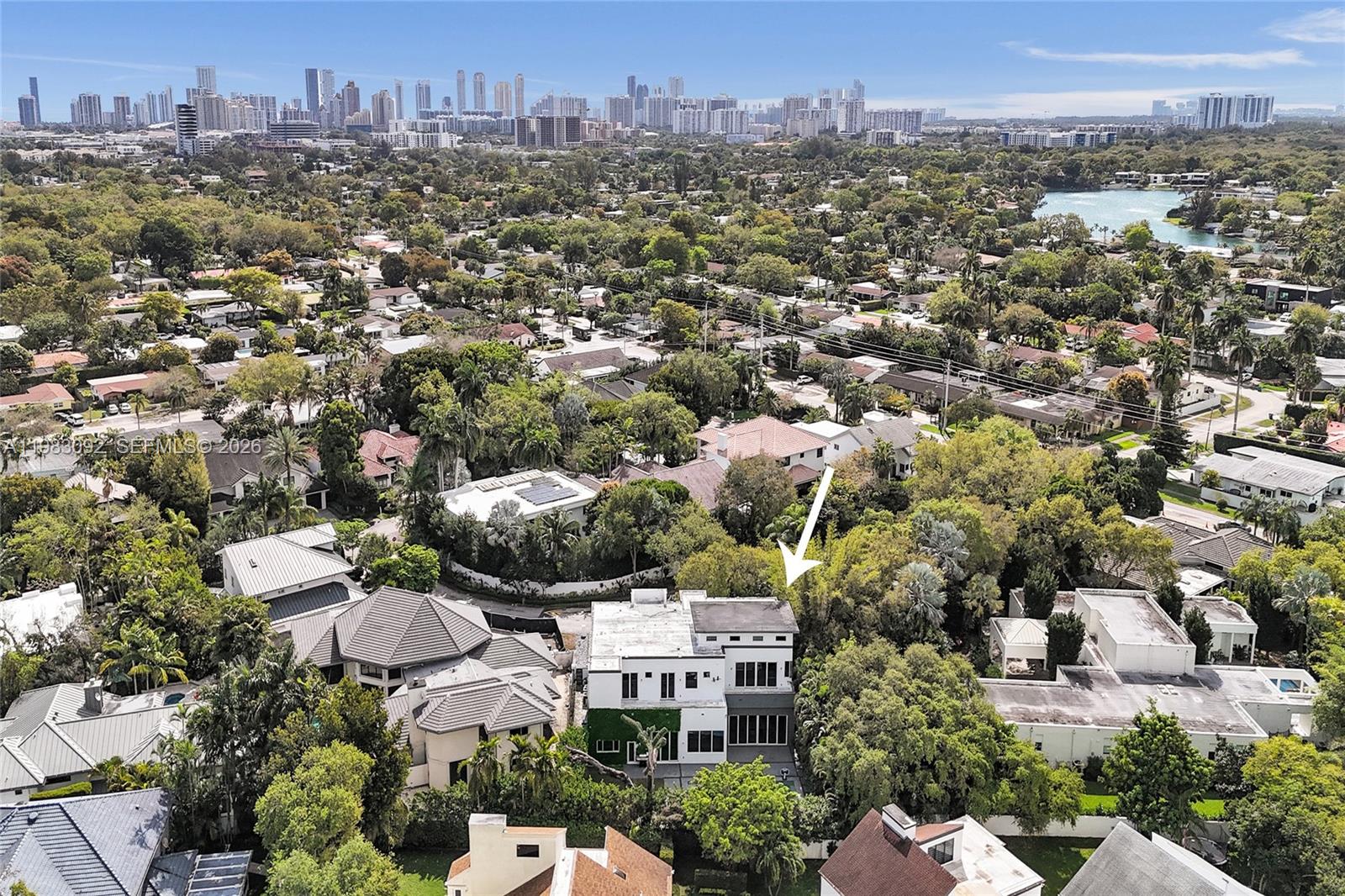 An aerial view shows a modern white house surrounded by lush trees and suburban homes — 19914 NE 19th Ct, Miami FL 33179, MIAMI, FL