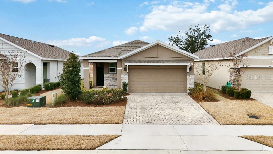 A single-story suburban house with a tan stucco exterior, stone accents, and a paved driveway — 5464 NW 46TH LANE ROAD, OCALA, FL