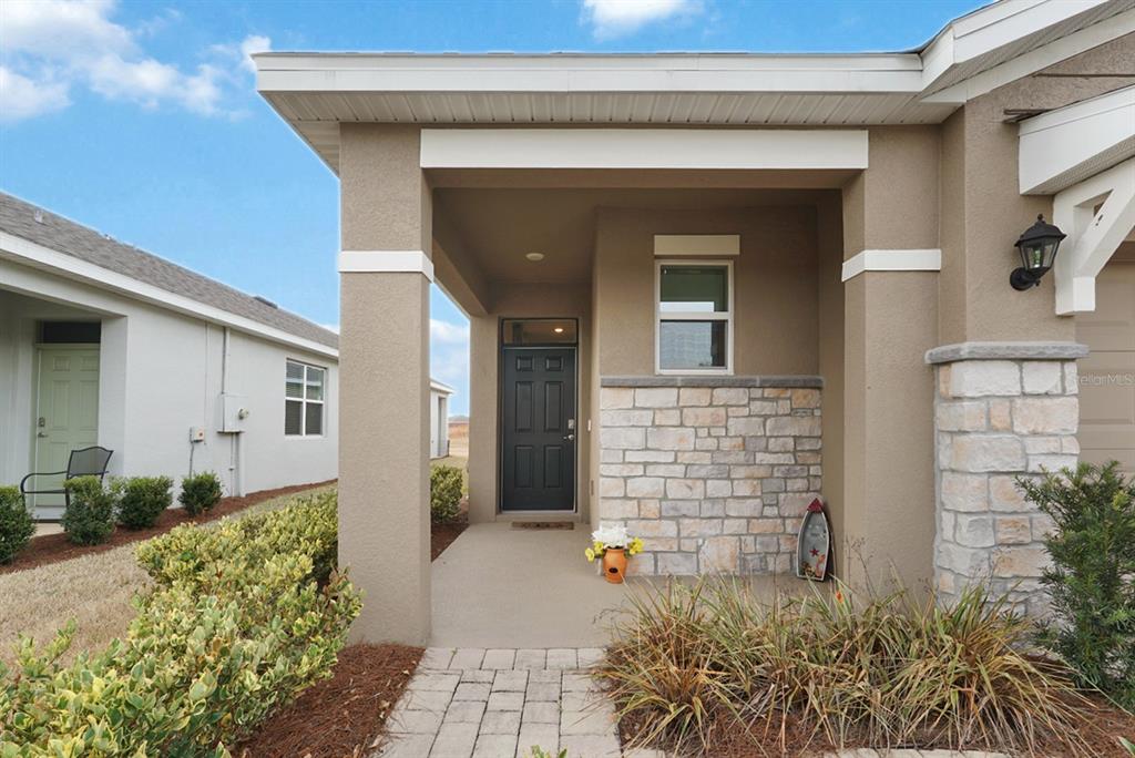 A covered front porch with a stone facade, a dark door, and a paved walkway — 5464 NW 46TH LANE ROAD, OCALA, FL