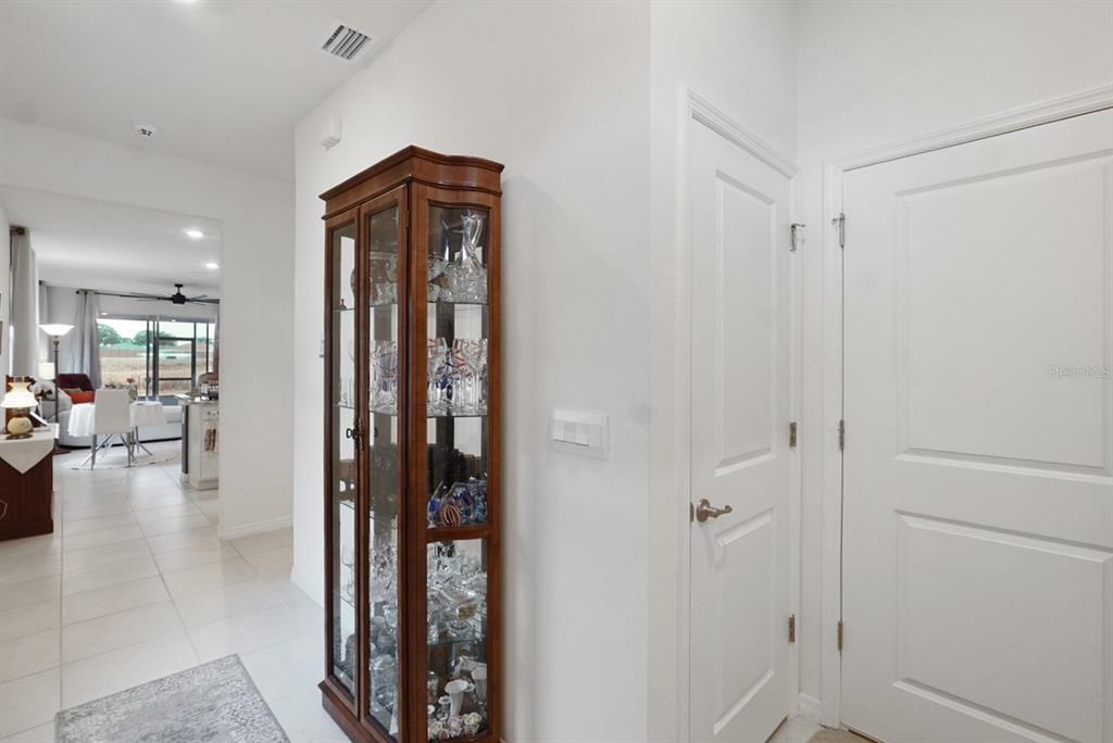 A hallway features a wooden curio cabinet, white walls, tiled floors, and two closed doors — 5464 NW 46TH LANE ROAD, OCALA, FL