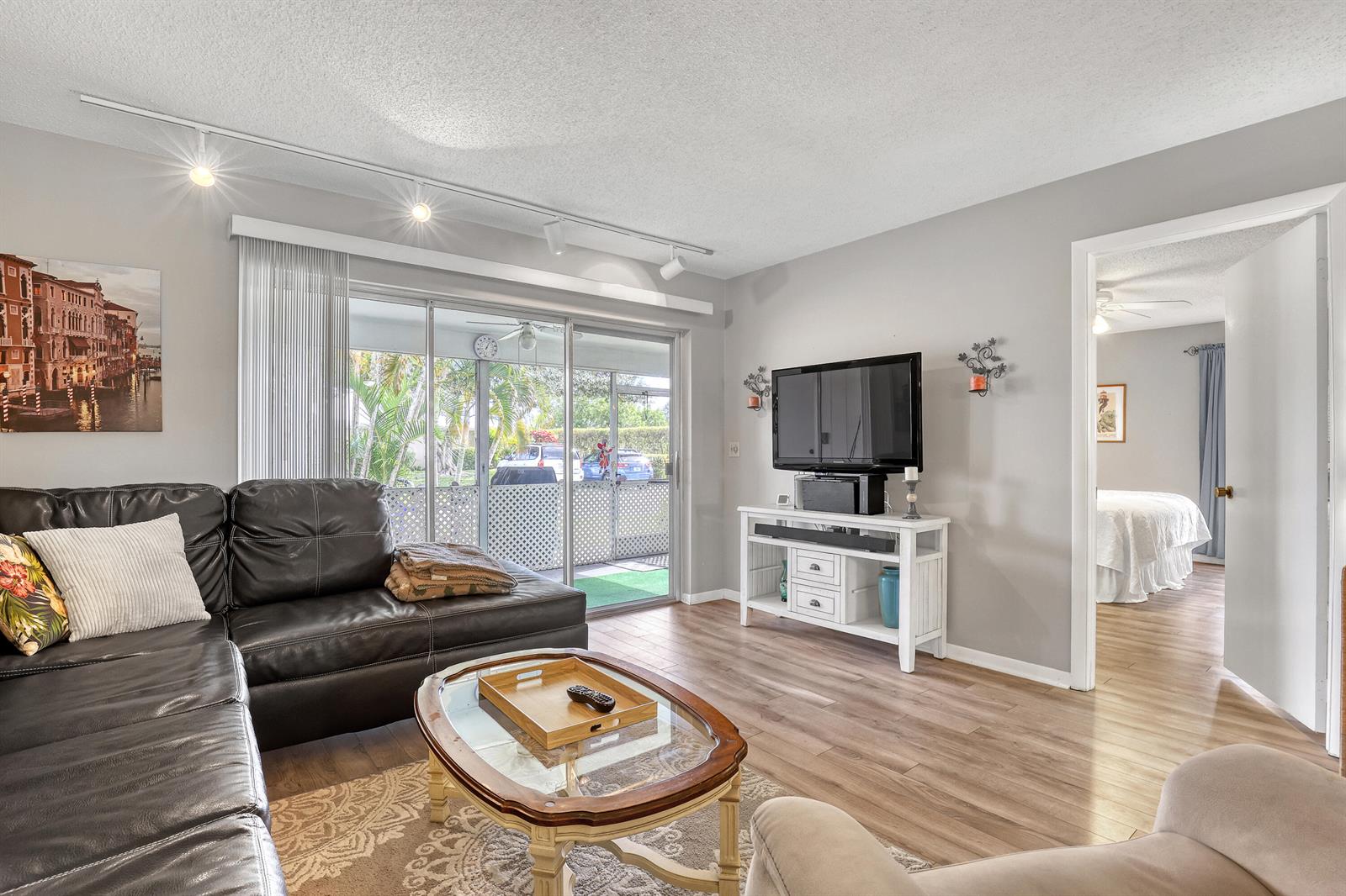 A living room features a dark leather sectional, a glass-topped coffee table, and sliding doors — 553 Covered Bridge Boulevard, Lake Worth FL 33467, LAKE WORTH, FL
