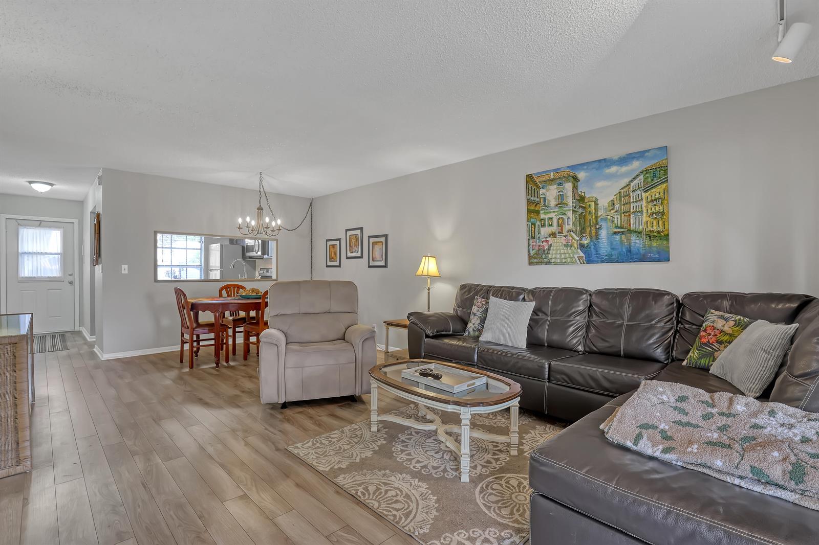 A living room with wood-look flooring, a dark leather sectional, and an adjacent dining area — 553 Covered Bridge Boulevard, Lake Worth FL 33467, LAKE WORTH, FL