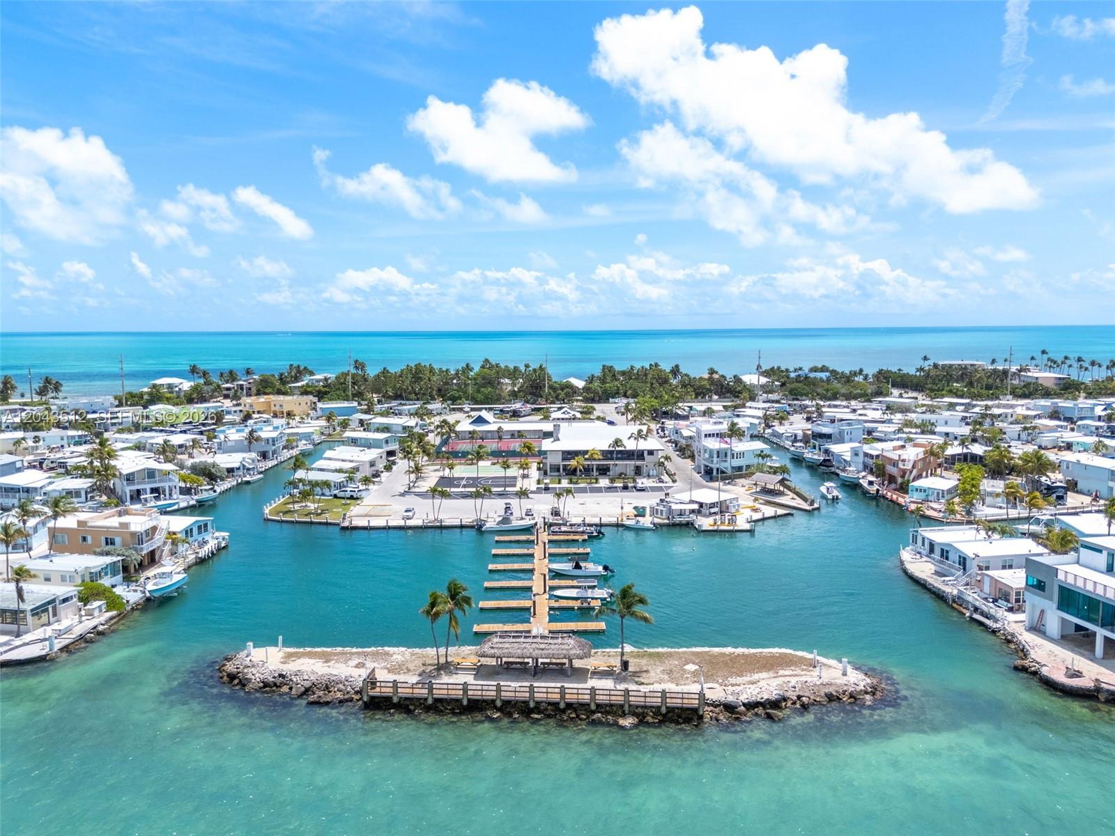 An aerial view shows a marina with a central dock, palm trees, and surrounding waterfront homes — 65821 Overseas Hwy #291, Long Key FL 33001, LONG KEY, FL