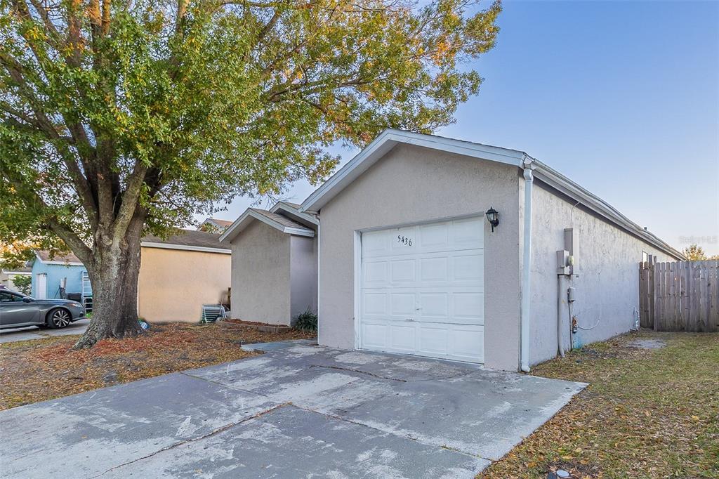 A single-story house with a white garage door and a concrete driveway under a large tree — 5436 WOOD CROSSING STREET, ORLANDO, FL