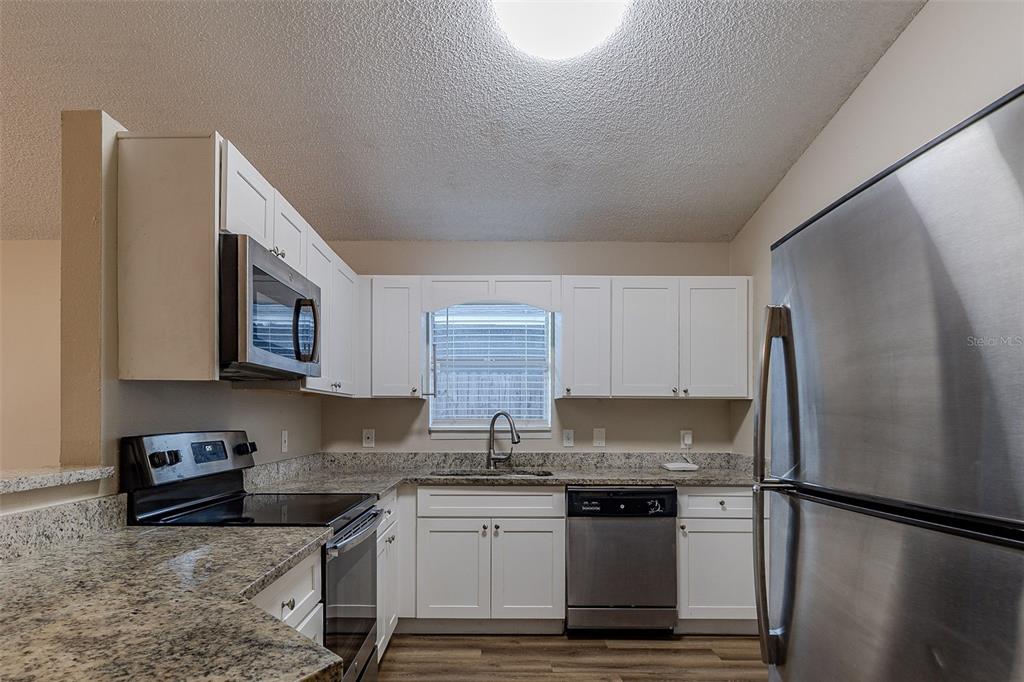 A kitchen features white cabinets, granite countertops, stainless steel appliances, and a window above the sink — 5436 WOOD CROSSING STREET, ORLANDO, FL