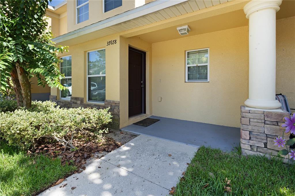 The exterior of a tan stucco home features a covered entryway with a stone pillar — 37678 AARALYN ROAD UNIT 57, ZEPHYRHILLS, FL