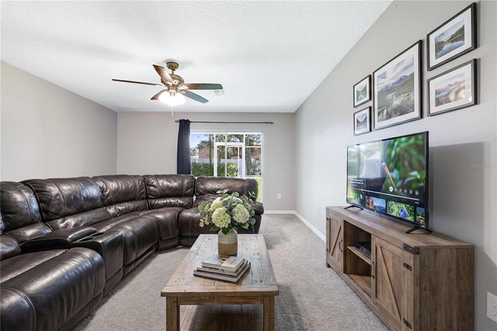 A living room features a dark leather sectional, a wooden coffee table, and a television — 37678 AARALYN ROAD UNIT 57, ZEPHYRHILLS, FL
