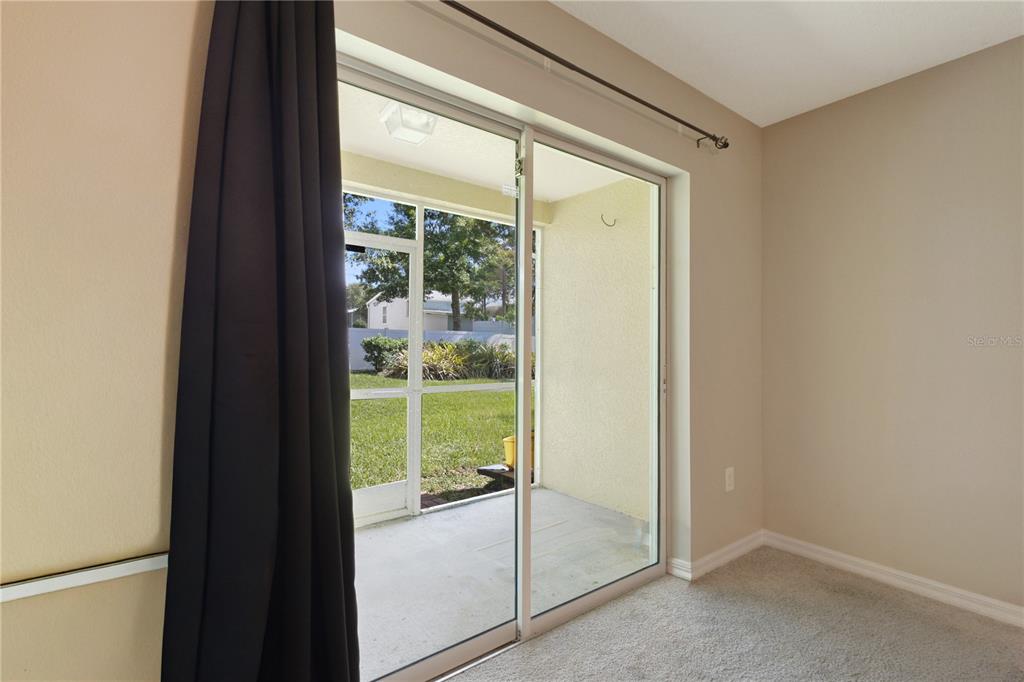 A carpeted room features a sliding glass door opening to a screened-in patio — 37678 AARALYN ROAD UNIT 57, ZEPHYRHILLS, FL