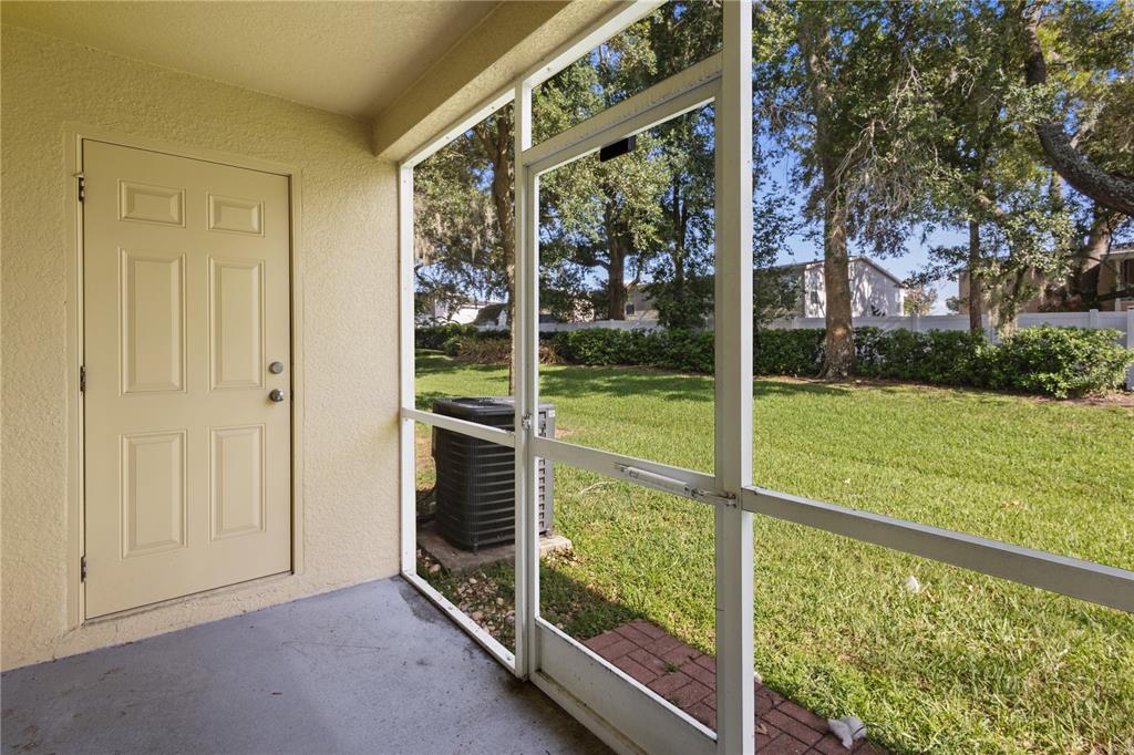 A screened-in patio features a beige door, concrete flooring, and a view of the lawn — 37678 AARALYN ROAD UNIT 57, ZEPHYRHILLS, FL