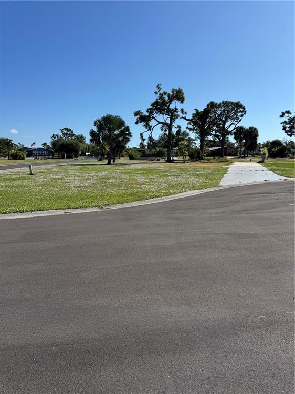 A vacant, grassy lot features a concrete driveway and several mature trees under a clear sky — 3303 DOVE LANE, ENGLEWOOD, FL