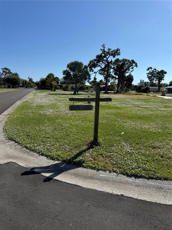 A wooden sign labeled Dove Lane stands on a grassy lot next to a road — 3303 DOVE LANE, ENGLEWOOD, FL