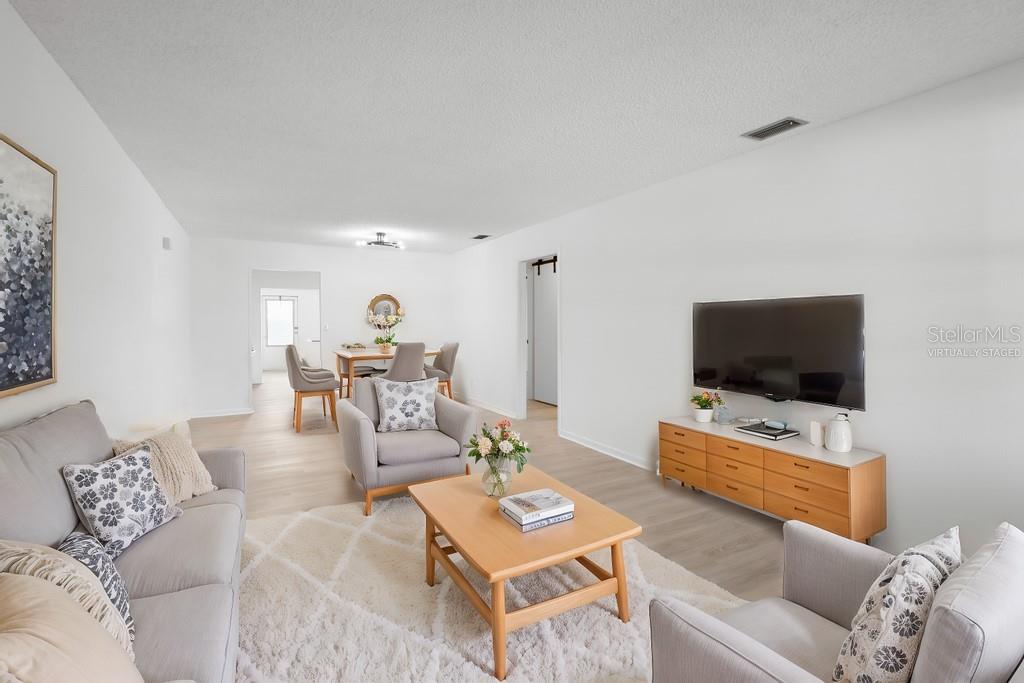 A virtually staged living room features light wood flooring, a television, and neutral furniture — 11200 102ND AVENUE UNIT 74, SEMINOLE, FL