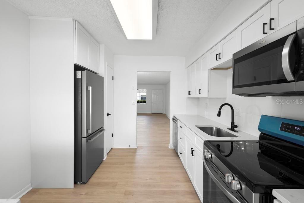 A galley-style kitchen features white cabinets, stainless steel appliances, and light wood-look flooring — 11200 102ND AVENUE UNIT 74, SEMINOLE, FL