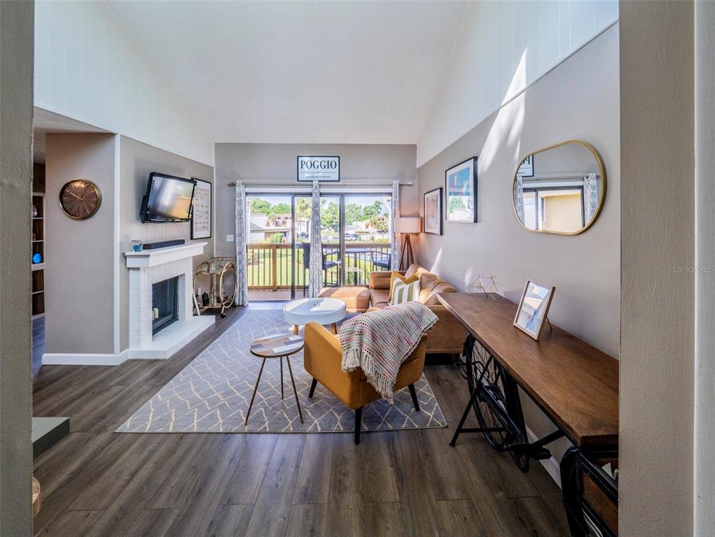 A living room features a fireplace, vaulted ceiling, wood-look flooring, and a sliding glass door — 1051 S HIGHLAND STREET UNIT 7E, MOUNT DORA, FL