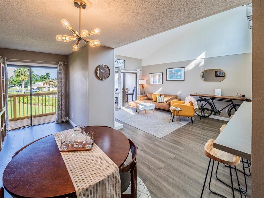 An open-concept living and dining area features wood-look flooring, a vaulted ceiling, and a balcony — 1051 S HIGHLAND STREET UNIT 7E, MOUNT DORA, FL