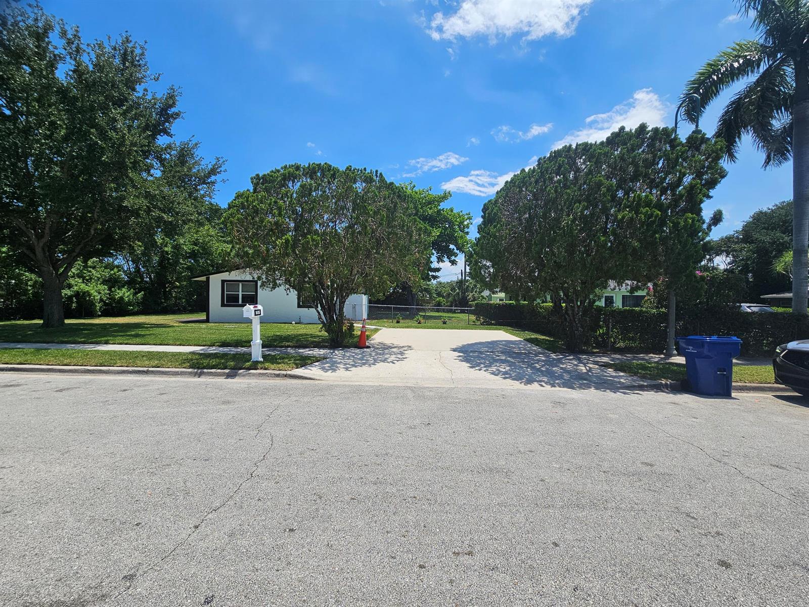 A white house with a concrete driveway sits behind two large trees on a sunny day — 1605 W 10th Street, Riviera Beach FL 33404, RIVIERA BEACH, FL