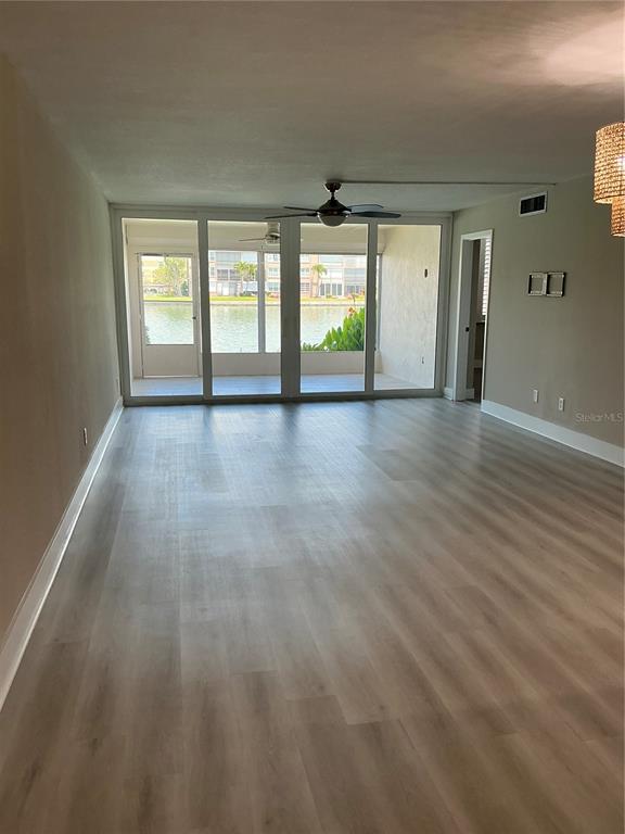An empty living room with light wood-look flooring leads to a screened-in porch overlooking water — 7645 SUN ISLAND DRIVE S UNIT 101, SOUTH PASADENA, FL