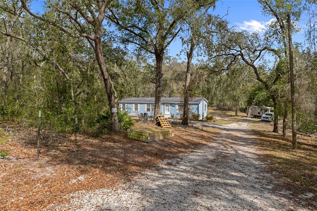 A light blue mobile home sits on a wooded lot with a dirt driveway — 11881 SW 45TH STREET, WEBSTER, FL