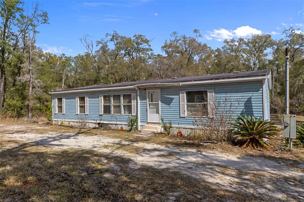 A light blue single-wide mobile home sits on a dirt lot surrounded by trees — 11881 SW 45TH STREET, WEBSTER, FL