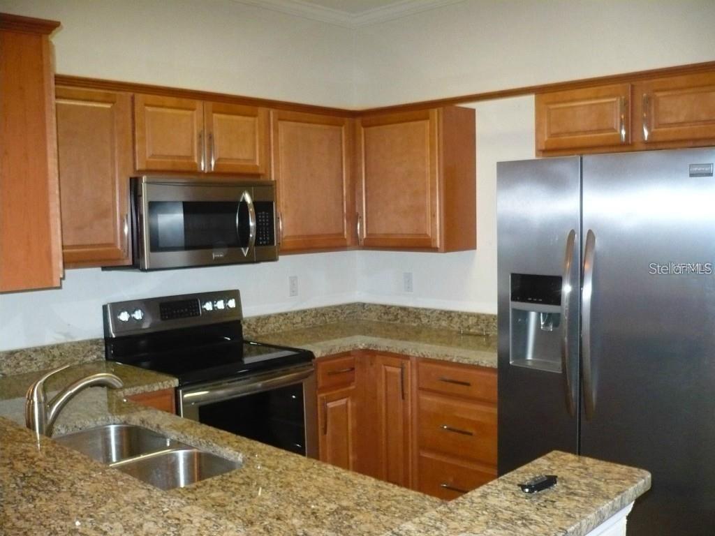 A kitchen with wooden cabinets, granite countertops, and stainless steel appliances — 2530 LANCIEN COURT UNIT 2, ORLANDO, FL