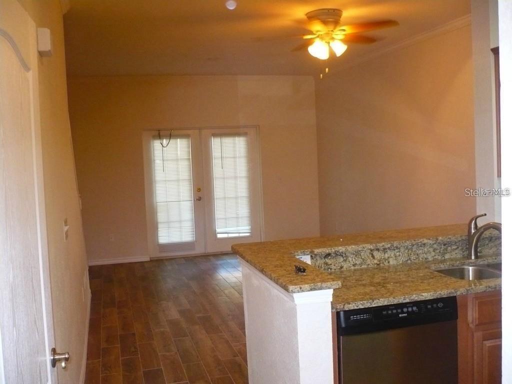 A kitchen with granite countertops and a dishwasher overlooks a room with wood-look flooring — 2530 LANCIEN COURT UNIT 2, ORLANDO, FL