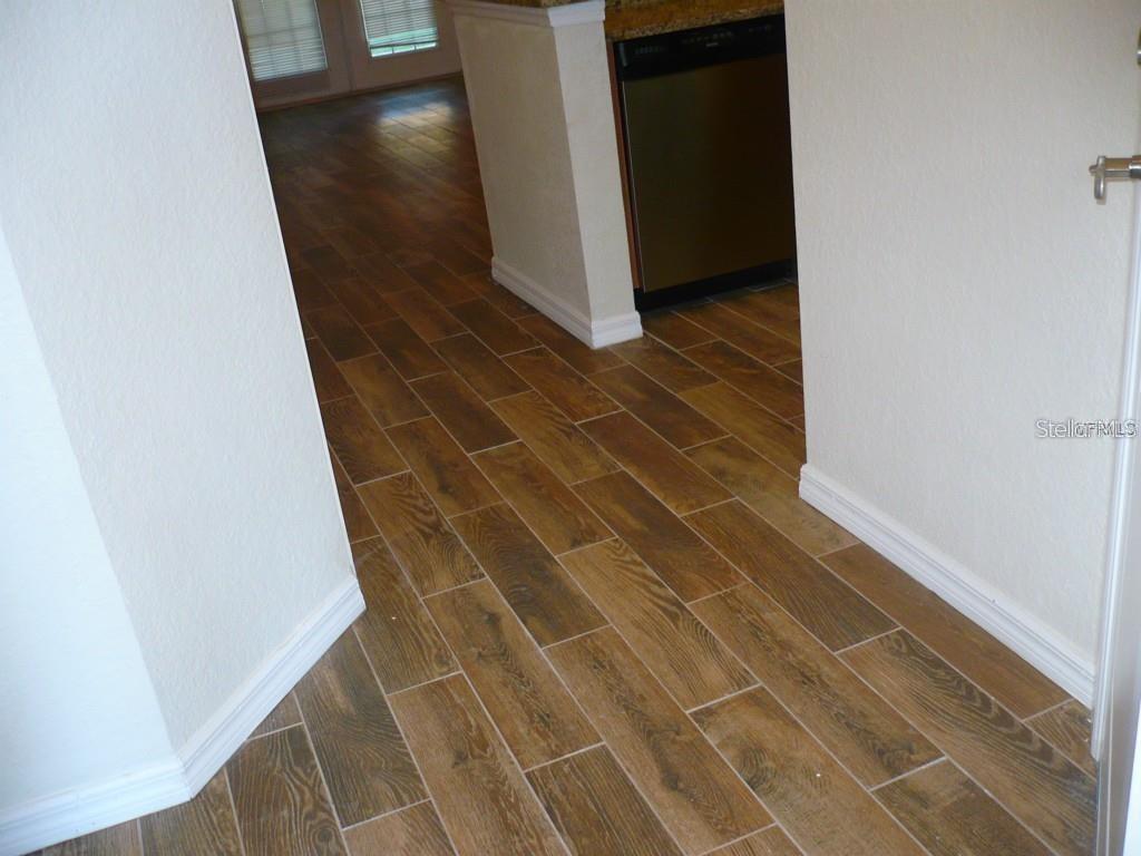 A hallway with wood-look tile flooring leads toward a kitchen with a stainless steel dishwasher — 2530 LANCIEN COURT UNIT 2, ORLANDO, FL
