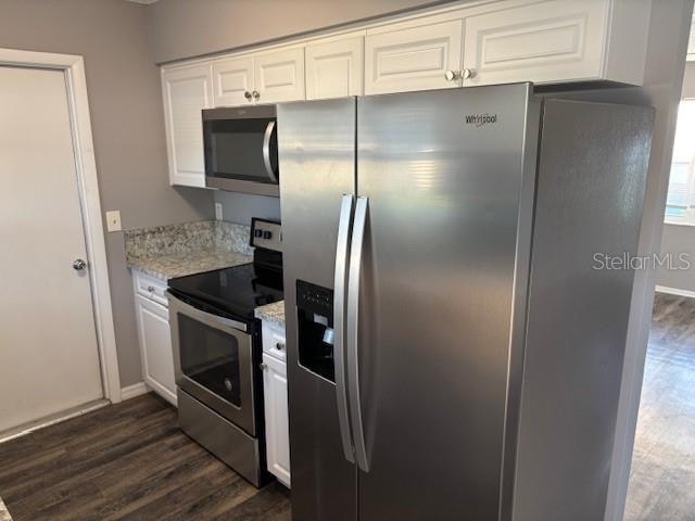 A kitchen features stainless steel appliances, white cabinets, and granite countertops over wood-look flooring — 13233 GRAND TERRACE DRIVE, GRAND ISLAND, FL