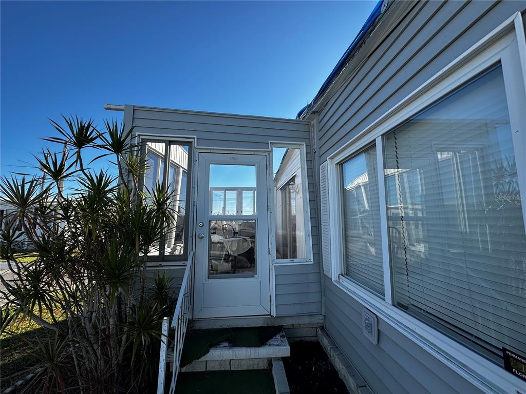 An exterior view of a mobile home entrance with gray siding, a storm door, and windows — 361 TAMPICO DRIVE, PALMETTO, FL