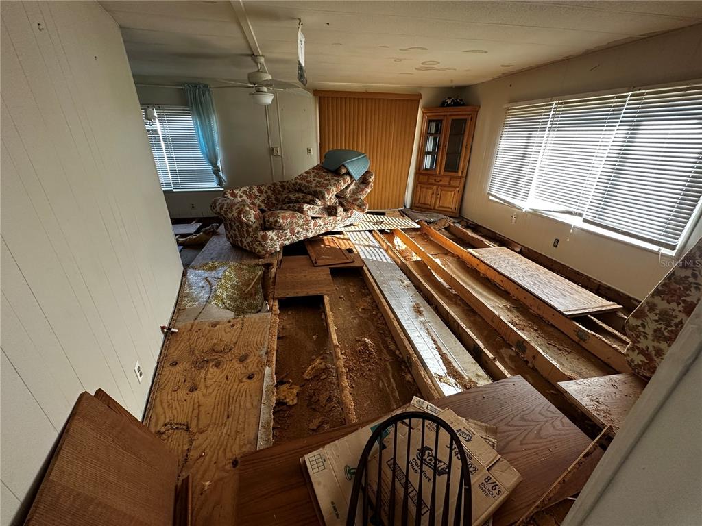 A living room with exposed floor joists, missing subflooring, and a floral sofa — 361 TAMPICO DRIVE, PALMETTO, FL