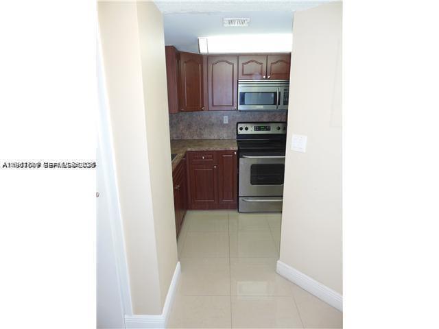 A galley-style kitchen features wood cabinets, stainless steel appliances, and light-colored tile flooring — 8335 SW 152 AV # 308, Miami FL 33193, MIAMI, FL