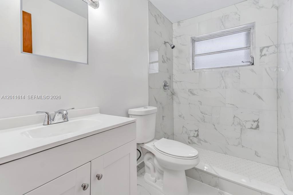 A bathroom features a white vanity, a toilet, and a walk-in shower with marble-look tiles — 519 NW 10th Ave, Miami FL 33136, MIAMI, FL