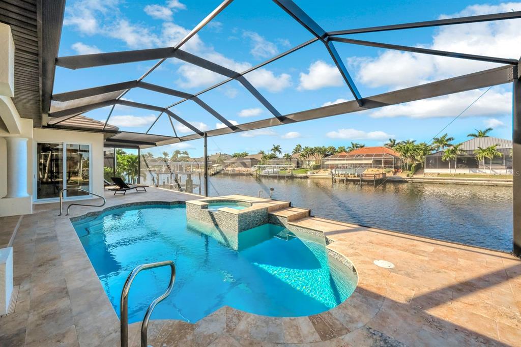 A screened-in pool and hot tub overlook a canal with neighboring houses in the background — 4518 SW 22ND PLACE, CAPE CORAL, FL