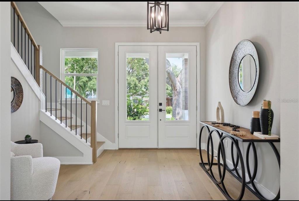 A bright entryway features light wood floors, a staircase with black railings, and double glass doors — 6705 S HIMES AVENUE, TAMPA, FL