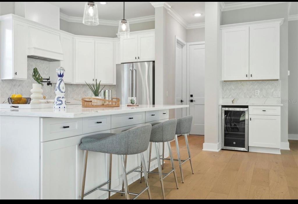 A modern white kitchen features a large island with gray bar stools and hardwood floors — 6705 S HIMES AVENUE, TAMPA, FL