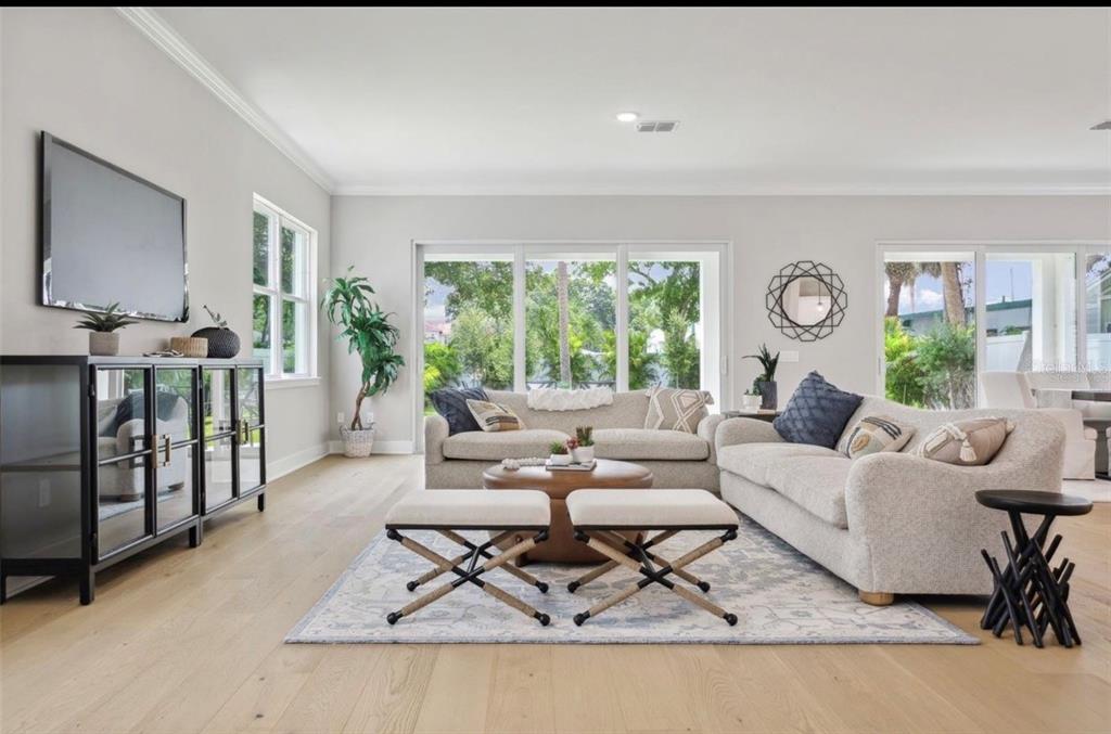 A bright living room features light wood floors, a sectional sofa, and large sliding glass doors — 6705 S HIMES AVENUE, TAMPA, FL