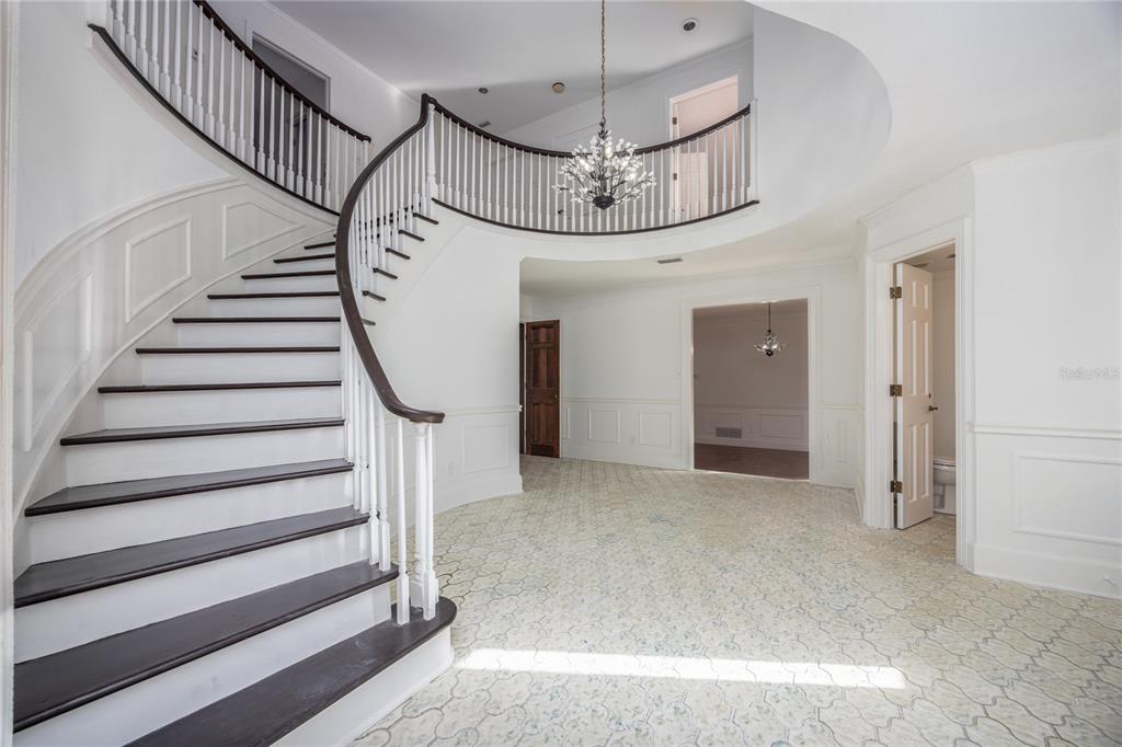 A grand foyer features a curved staircase with dark wood treads and a white railing — 1701 NW 30TH TERRACE, GAINESVILLE, FL