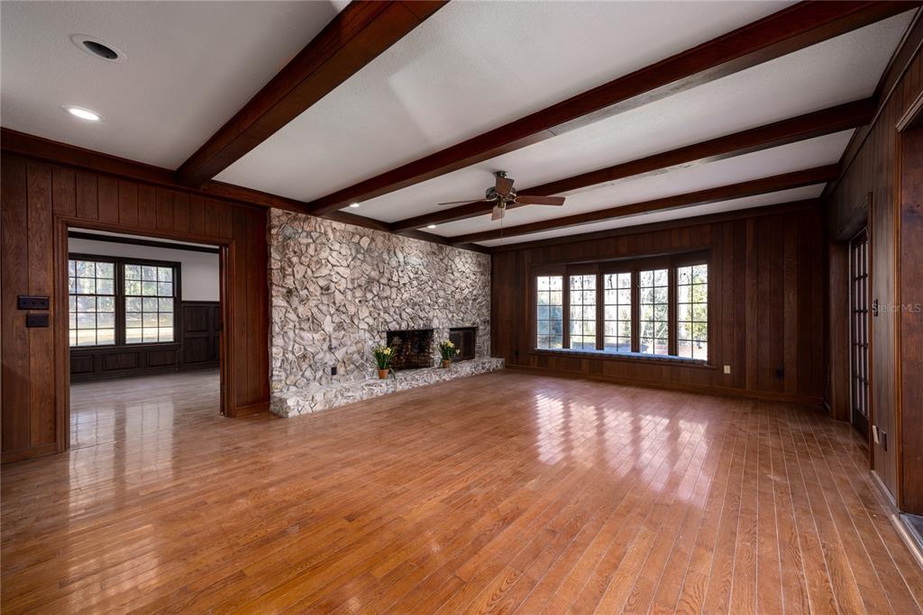 A living room features wood-paneled walls, a stone fireplace, exposed ceiling beams, and hardwood floors — 1701 NW 30TH TERRACE, GAINESVILLE, FL