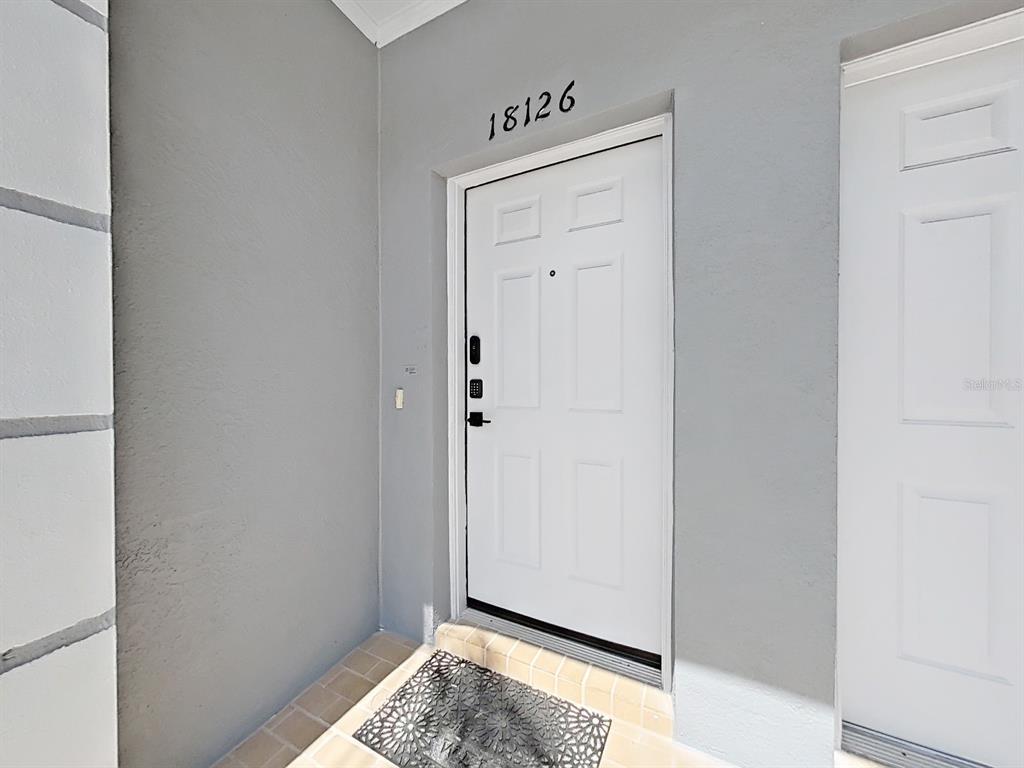 A white front door with a keypad lock is set into a gray exterior wall — 18126 PARADISE POINT DRIVE, TAMPA, FL