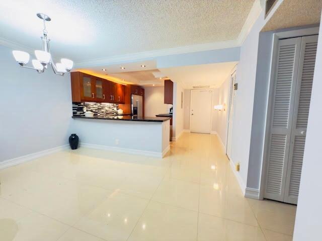 An open-concept dining area and kitchen with tile flooring, wooden cabinets, and a chandelier — 3080 N Course Drive # 202, Pompano Beach FL 33069, POMPANO BEACH, FL